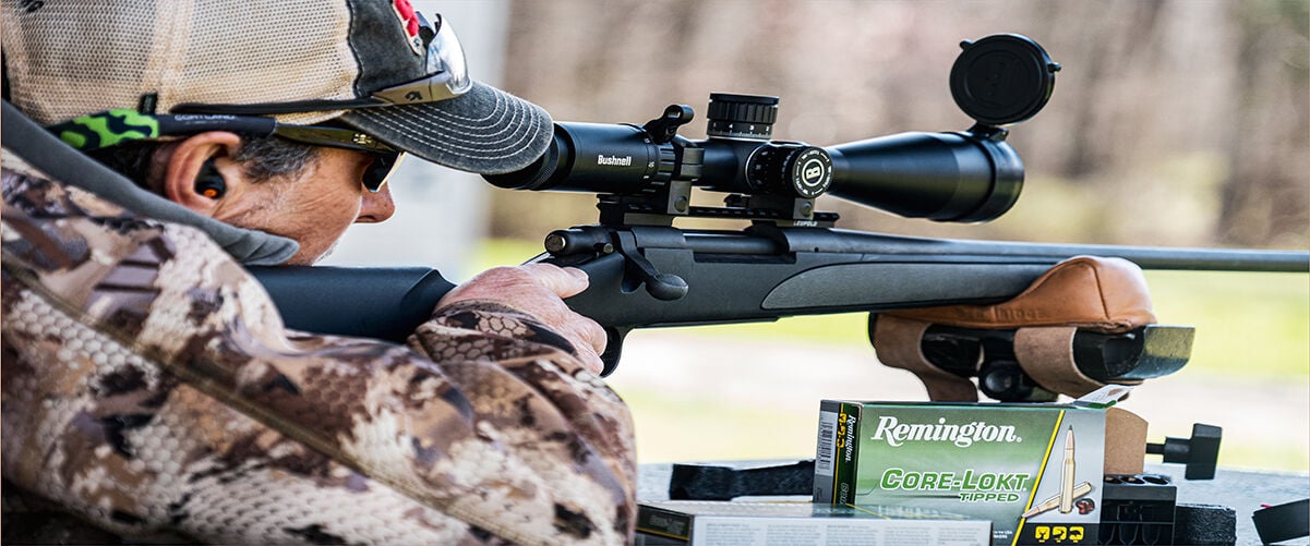 Man looking through rifle scope with box of Core-Lokt